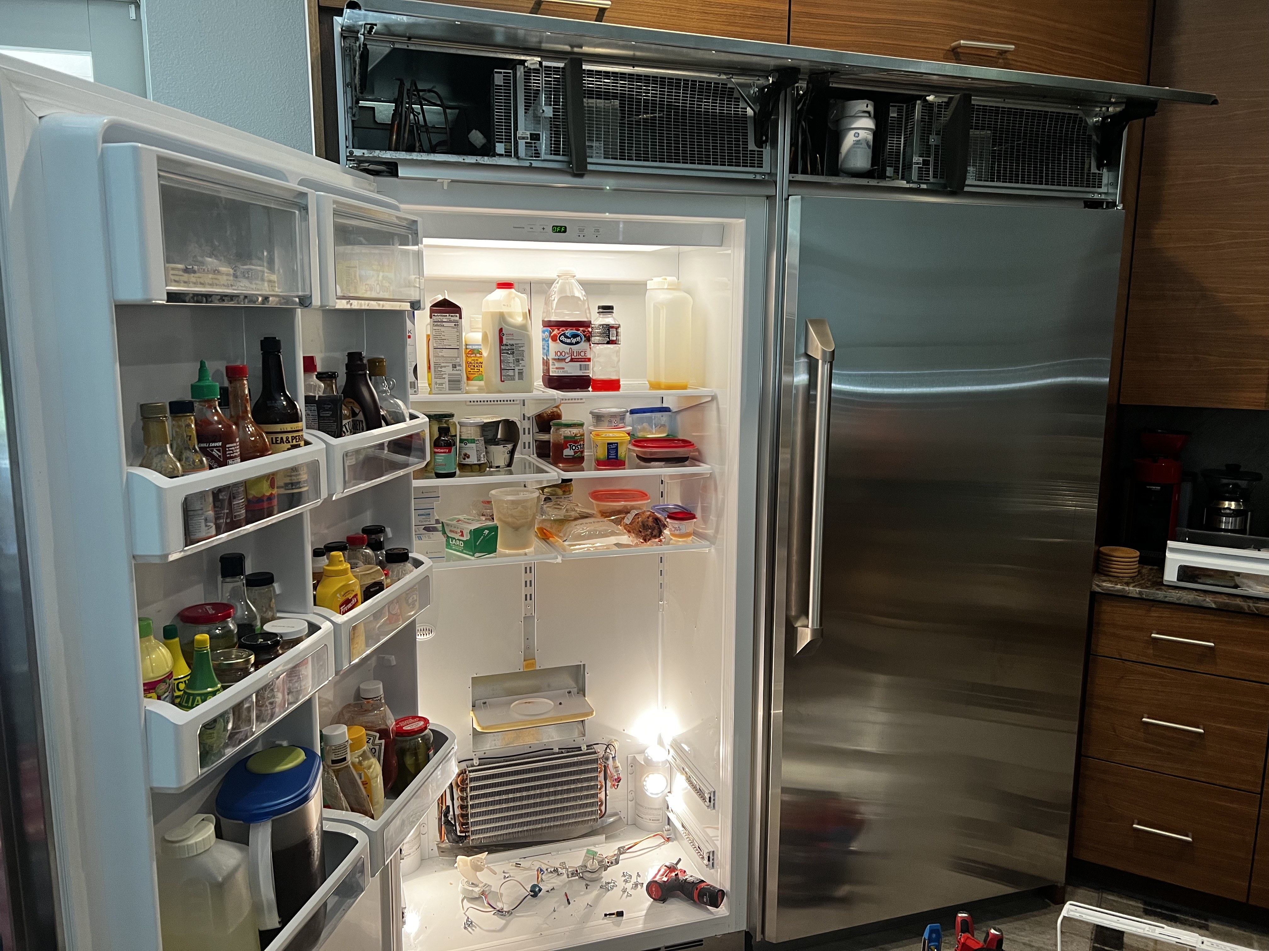 GE Monogram french door refrigerator open showing evaporator coils exposed at bottom during repair — New Port Richey