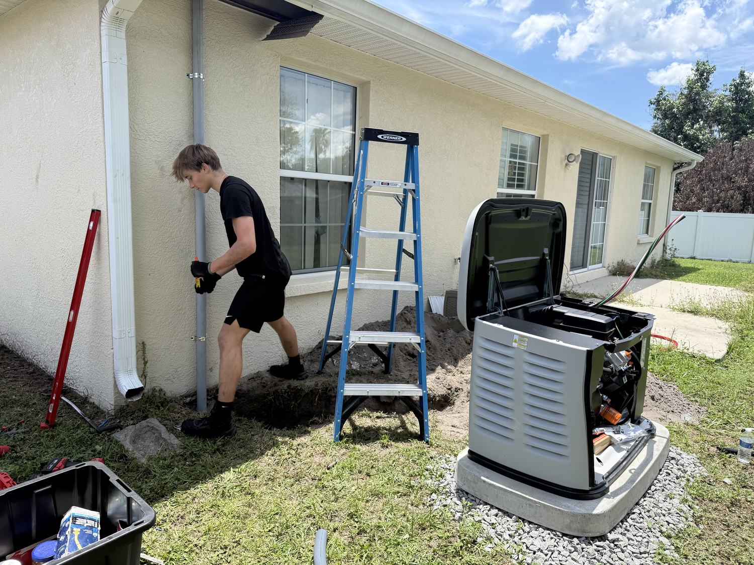 Electrician running conduit up an exterior wall toward the transfer switch location, generator staged in the background, Tampa Bay