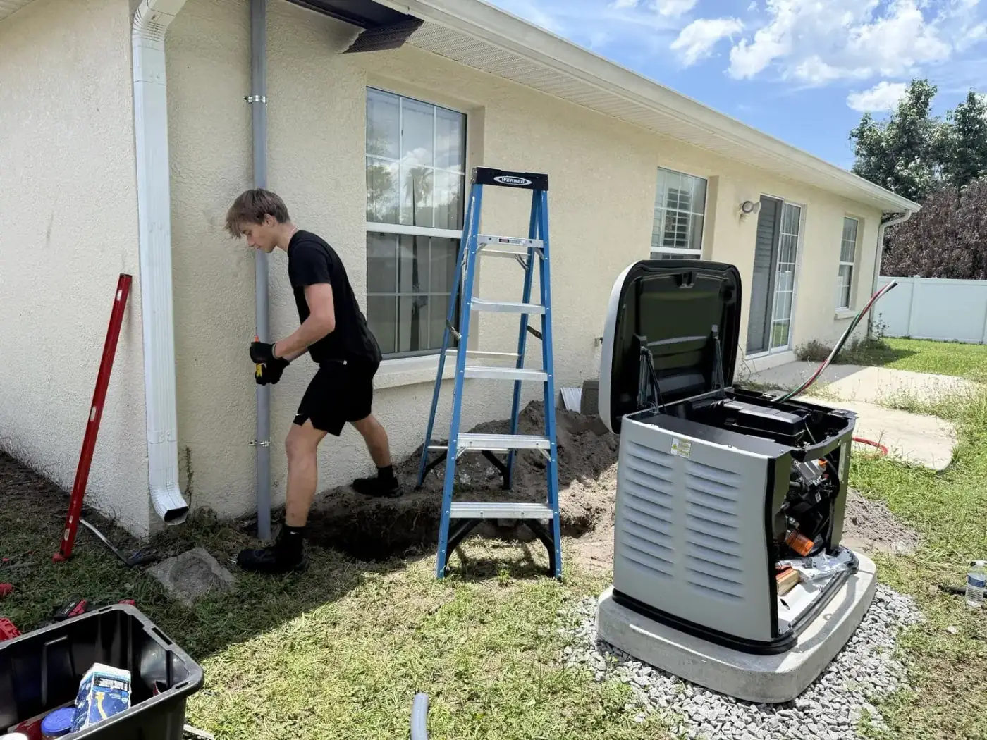 Electrician running conduit up an exterior wall toward the transfer switch location, generator staged in the background, Tampa Bay