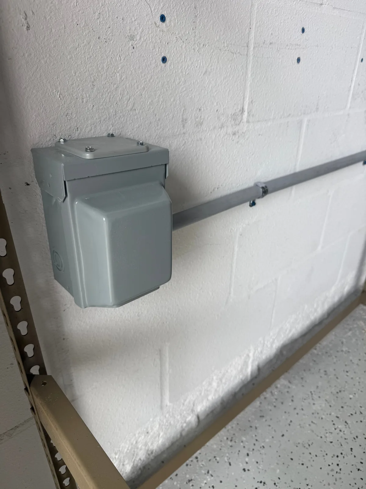Closed gray raintight NEMA 14-50 enclosure mounted on a block garage wall with EMT conduit run to the panel — Tampa Bay EV charging circuit