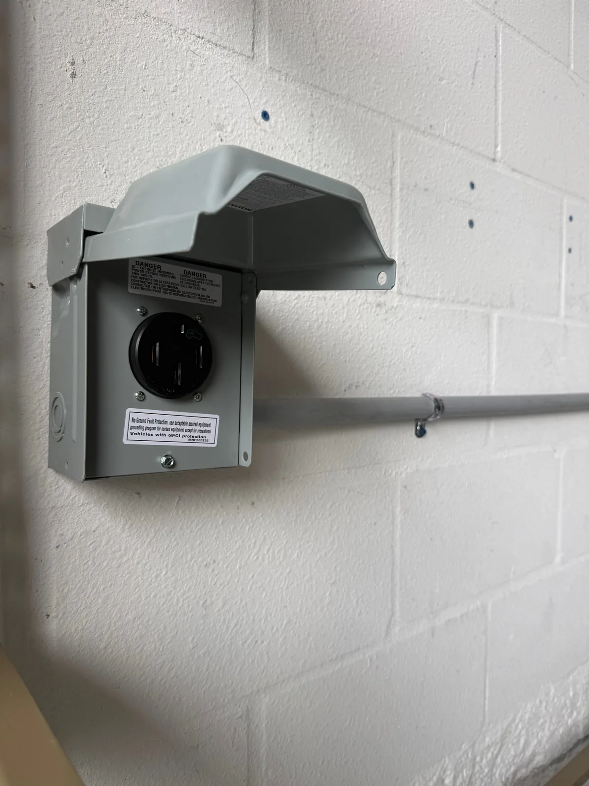 NEMA 14-50 outlet in a gray raintight metal enclosure with the cover open, fed by EMT conduit across a painted block garage wall in Tampa Bay